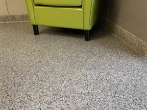 A close-up image of an epoxy floor coating with PVA chips. A green chair can be seen in the corner.