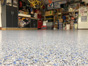 A garage with a lot of items on racks in the corner has an epoxy concrete floor coating.