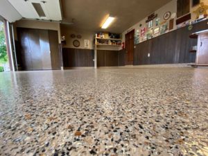 A large garage with wall-to-wall storage has an epoxy floor coating system with a stone-like finish.