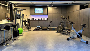 A basement with an epoxy floor coating has a full gym, wall-to-wall storage, and a built-in bar.