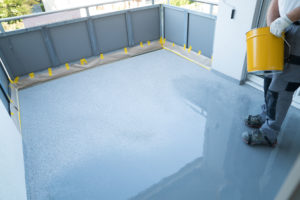 A construction worker renovates balcony floor and spreads chip floor covering on resin and glue coating before applying water sealant