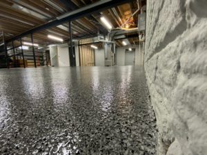 Black, grey, and white speckled epoxy floor coating on the floor of a large basement.