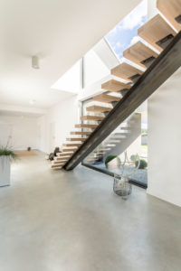 Designed wooden stairs in spacious white apartment with a coated concrete floor