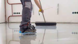 Person wear shoe spike spreads epoxy floor coating onto a concrete floor