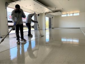 Two people at work installing an epoxy floor coating in a large garage with white walls